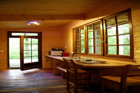 Wooden interior of Ecolodge «en Sequoia» in France, large windows, open door, and cozy kitchen space.