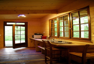 Wooden interior of Ecolodge «en Sequoia» in France, large windows, open door, and cozy kitchen space.