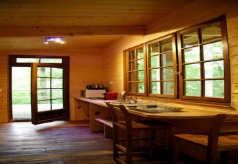 Wooden interior of Ecolodge «en Sequoia» in France, large windows, open door, and cozy kitchen space.