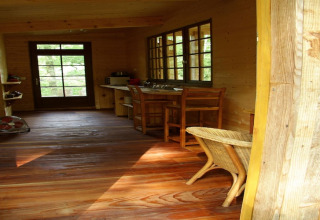 Interior of Ecolodge «en Sequoia» cabin in France with wooden floor, furniture, and large windows.