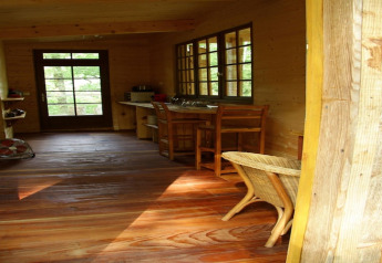 Interior of Ecolodge «en Sequoia» cabin in France with wooden floor, furniture, and large windows.