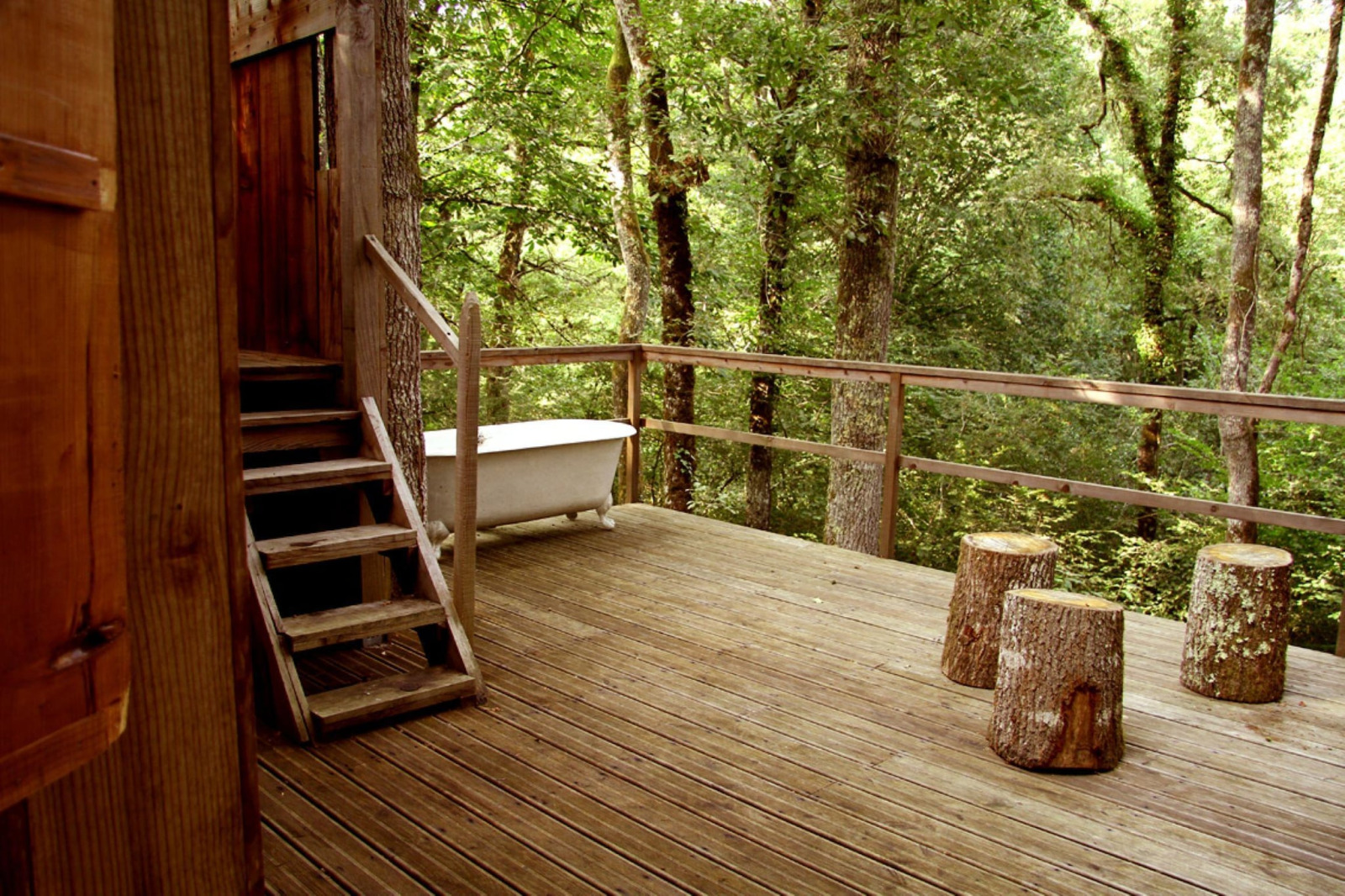 Houten terras van Ecolodge «en Sequoia» in Frankrijk met buitenbad en boomstamkrukken in het bos.