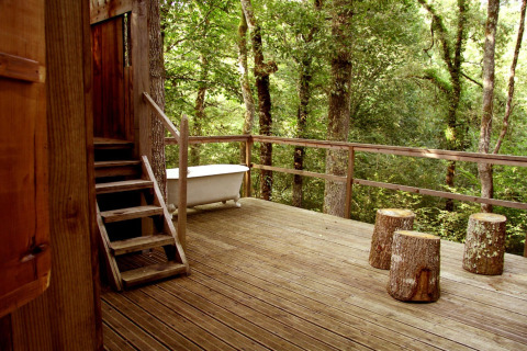 Wooden deck at Ecolodge «en Sequoia» in France with outdoor bathtub and stump seats amidst forest trees.