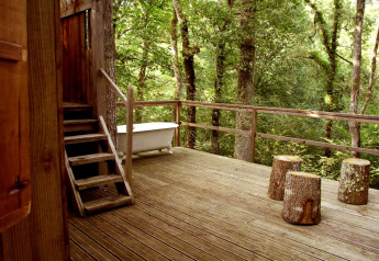 Holzterrasse der Ecolodge «en Sequoia» in Frankreich mit Badewanne und Baumstumpfhockern im Wald.