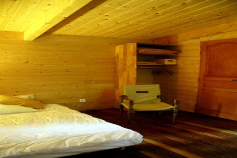Bedroom at Ecolodge «en Sequoia» in France, with wooden interior, bed, chair, closet, and door.