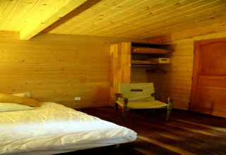 Bedroom at Ecolodge «en Sequoia» in France, with wooden interior, bed, chair, closet, and door.
