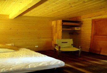 Bedroom at Ecolodge «en Sequoia» in France, with wooden interior, bed, chair, closet, and door.