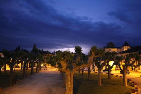 Evening view of tree-lined square at Ecolodge «en Sequoia» in France, lit by warm outdoor lights.