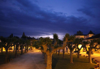 Evening view of tree-lined square at Ecolodge «en Sequoia» in France, lit by warm outdoor lights.