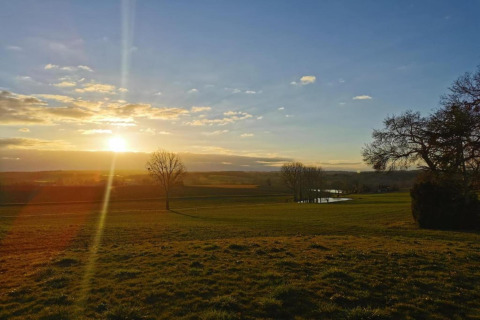Sunset over a tranquil meadow at Ecolodge «en Sequoia» in France, with trees and a peaceful pond.