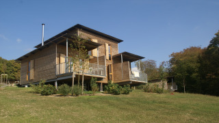 Moderna lodge in legno su una collina erbosa, circondata dalla natura e alberi sotto un cielo sereno.