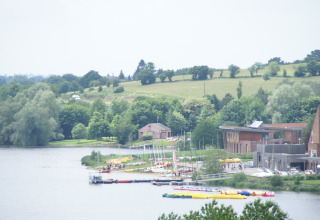Zicht op een lodge aan het meer met boten, steigers en gebouwen tussen groene heuvels en bomen.