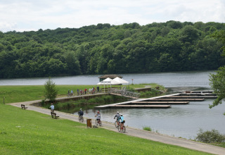 Fietsers rijden langs een meer met drijvende pontons en groene heuvels op de achtergrond bij een lodge.