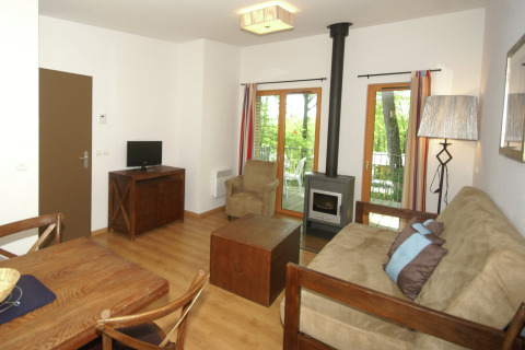 Woonruimte in een lodge met houten meubilair, kachel, tv en grote ramen naar het bosrijke balkon.