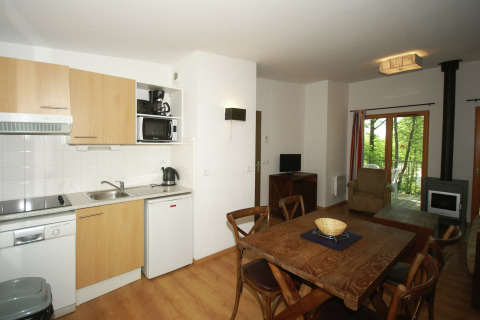 Heldere lodge-keuken met eettafel, houten meubels, houtkachel en zicht op het groene balkon.