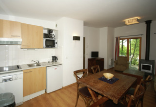 Heldere lodge-keuken met eettafel, houten meubels, houtkachel en zicht op het groene balkon.