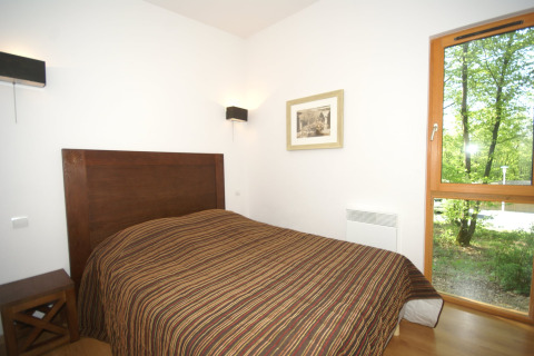 Lichte slaapkamer van een lodge met tweepersoonsbed, houten hoofdsteun en uitzicht op het groene bos buiten.