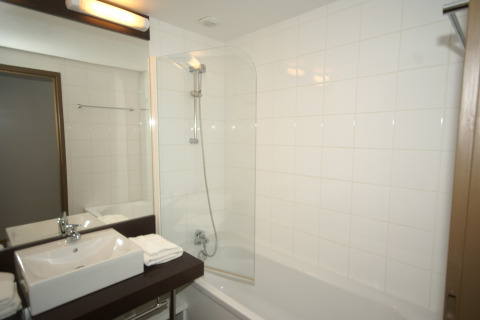 Moderne badkamer in een lodge met bad, witte tegels, rechthoekige wasbak en propere handdoeken op het blad.