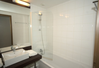 Moderne badkamer in een lodge met bad, witte tegels, rechthoekige wasbak en propere handdoeken op het blad.