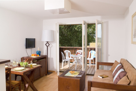 Gezellige lodge met eettafel, zetel en toegang tot balkon met tuinstoelen en mooi uitzicht buiten.