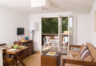 Gezellige lodge met eettafel, zetel en toegang tot balkon met tuinstoelen en mooi uitzicht buiten.