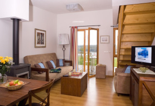 Lichte woonkamer in Les Hauts de Valjoly 4 in Frankrijk met zetel, tv, houtkachel en balkon.