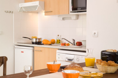Knusse lodge-keuken met ontbijt op tafel, vers brood, jus d’orange, croissants en groenten in zicht.