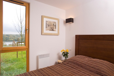Slaapkamer in de Les Hauts de Valjoly 4 lodge in Frankrijk met houten bed, raam en zicht op groene natuur.