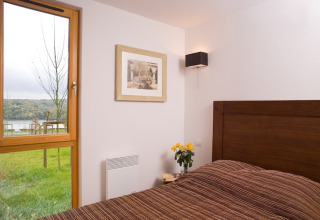 Slaapkamer in de Les Hauts de Valjoly 4 lodge in Frankrijk met houten bed, raam en zicht op groene natuur.