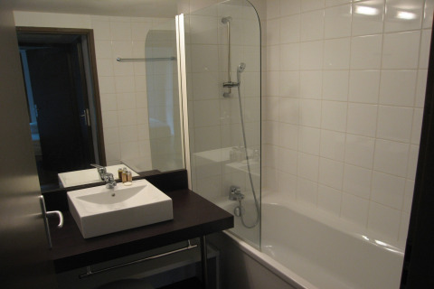 Moderne lodgebadkamer met vierkante wastafel, grote spiegel, bad-douchecombinatie en witte tegels.