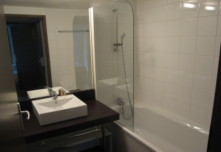 Moderne lodgebadkamer met vierkante wastafel, grote spiegel, bad-douchecombinatie en witte tegels.