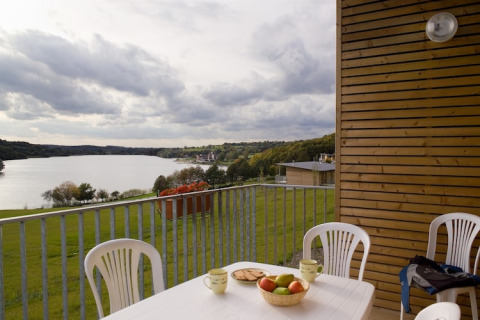 Uitzicht vanaf een lodge op een meer, terras met kunststof stoelen, fruitschaal en kopjes op tafel.
