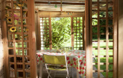 Vue à travers une pergola en bois sur une table à nappe fleurie dans le jardin de la Maison de vacances - LE PONCHEL.