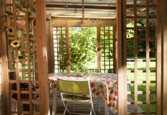Udsigt gennem en træpergola til et bord med blomstret dug i en solrig have ved Maison de vacances - LE PONCHEL.