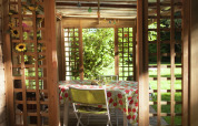 Blick durch eine Holzpergola auf einen Tisch mit Blumen-Tischdecke im Garten von Maison de vacances - LE PONCHEL.