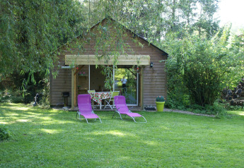 Cabaña llamada Maison de vacances - LE PONCHEL con dos tumbonas moradas en un jardín verde rodeado de árboles.