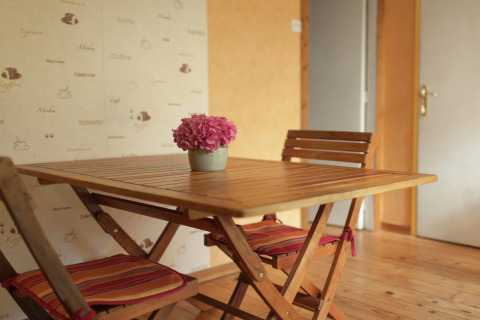 Træbord med to stole og en krukke med lyserøde blomster i Maison de vacances - LE PONCHEL, Frankrig.
