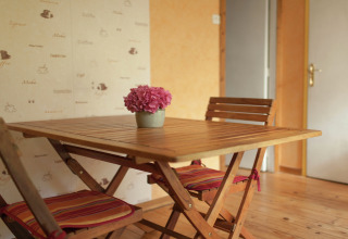 Træbord med to stole og en krukke med lyserøde blomster i Maison de vacances - LE PONCHEL, Frankrig.
