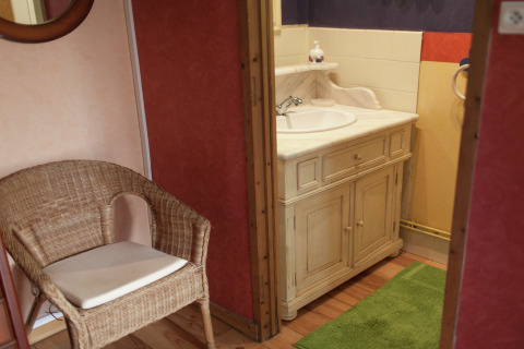 Baño acogedor con silla de mimbre, espejo y mueble de lavabo rústico en Maison de vacances - LE PONCHEL en Francia.