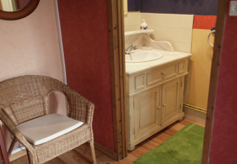 Baño acogedor con silla de mimbre, espejo y mueble de lavabo rústico en Maison de vacances - LE PONCHEL en Francia.