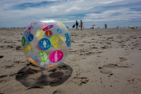 Pelota de playa colorida en la arena frente a Maison de vacances - LE PONCHEL en Francia, personas al fondo.