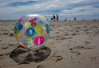 Colorful beach ball on the sand at Maison de vacances - LE PONCHEL in France, with people and umbrellas.