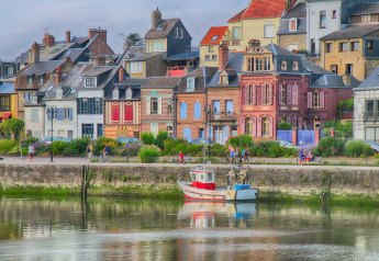 Casas coloridas junto al río en Le Ponchel, Francia, personas pasean por el malecón y un barco en el agua.