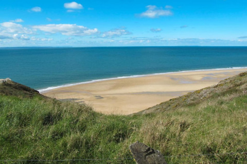 Kystudsigt fra Maison de vacances - LE PONCHEL i Frankrig med græs, sandstrand og blå himmel.