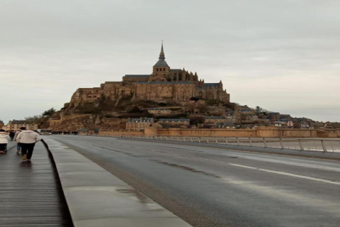 Et foto af Mont Saint-Michel i Frankrig, taget fra vejen, med mennesker gående i forgrunden.