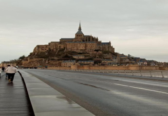 Foto di Mont Saint-Michel in Francia, scattata dalla strada con persone che camminano in primo piano.