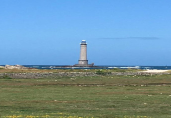 View of a tall lighthouse by the sea, photographed from the lawn near 'Maison de vacances - LE PONCHEL' in France.