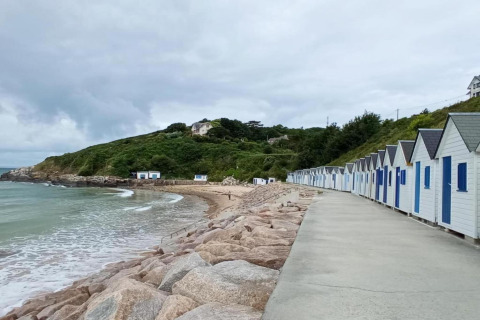 Casetas de playa junto al mar cerca de Maison de vacances - LE PONCHEL, Francia, con cielo nublado y colinas.
