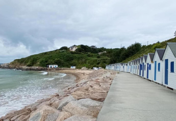 Casetas de playa junto al mar cerca de Maison de vacances - LE PONCHEL, Francia, con cielo nublado y colinas.
