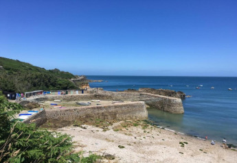 Steinwerft mit kleinen Booten und Hütten am Meer nahe Maison de vacances - LE PONCHEL, Frankreich, unter blauem Himmel.